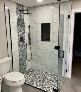Contemporary glass-enclosed shower with white marble-look wall tiles, mosaic accent, and pebble-style black-and-white floor for a modern look.