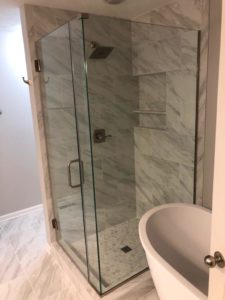 Elegant glass-enclosed shower with white marble-look wall tiles and hexagonal floor tiles, showcasing easy tile care and maintenance