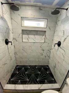 Modern shower with large white marble-look tiles, black geometric floor, and built-in niche