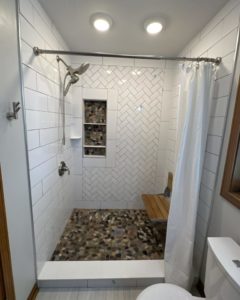 Shower remodel with pebble-like flooring and herringbone wall installed by a Noblesville tile installer.