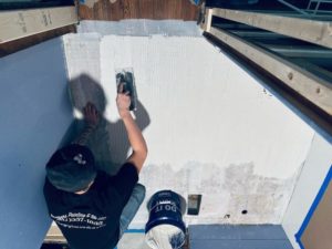 Worker applying mortar on a wall with a notched trowel, preparing the surface for tile installation.