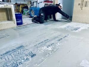 Worker applying mortar over cement backer boards on a floor during a tile installation preparation.